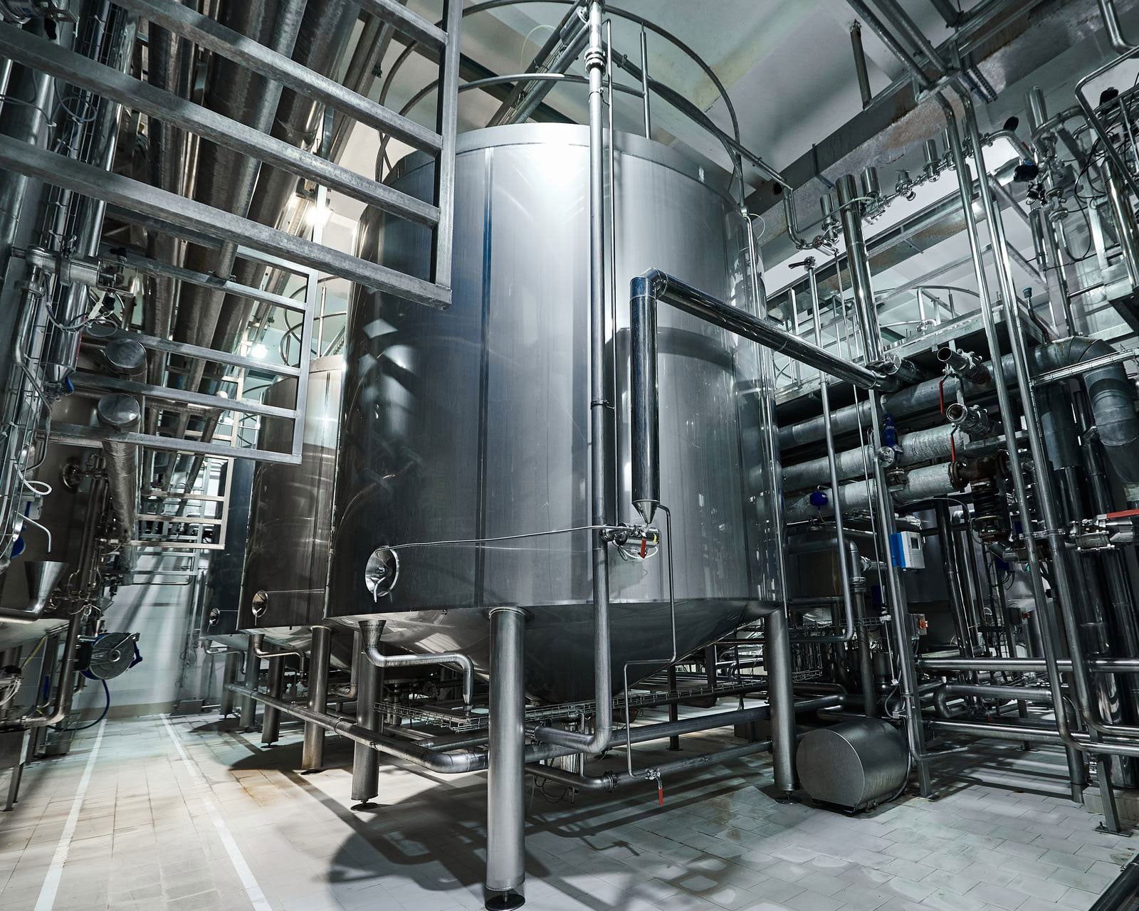 Large stainless steel process tank with surrounding piping and valves in an industrial production plant