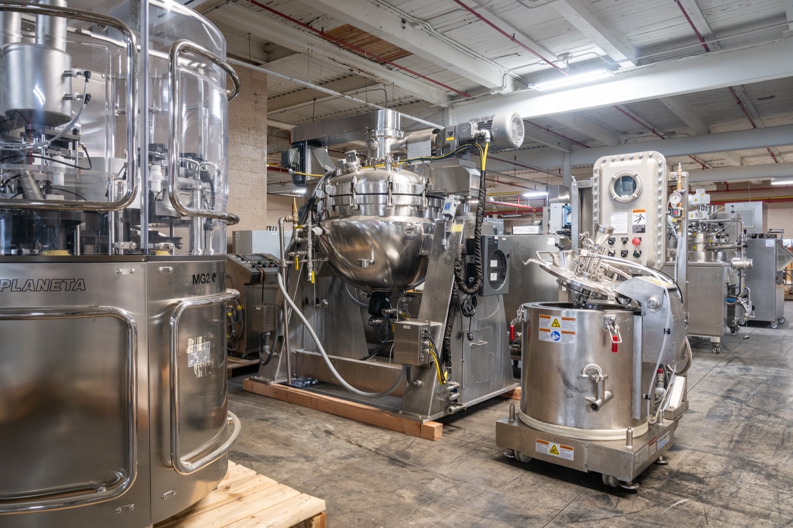An MG2 Planeta capsule filler beside a tilting jacketed kettle and other stainless steel process equipment on the Federal Equipment Company warehouse floor in Cleveland, OH