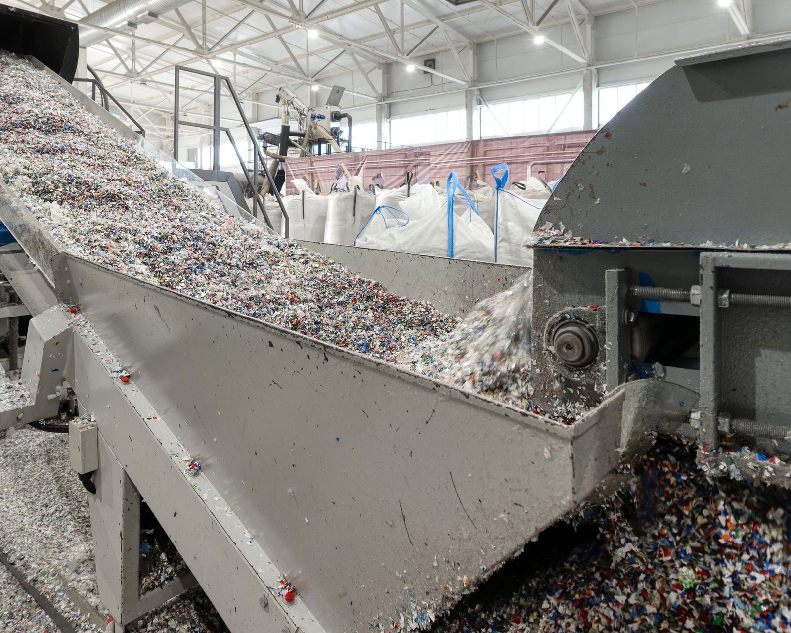 Shredded mixed plastic flake moving up an inclined conveyor into a discharge housing at a plastics recycling plant